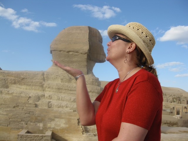 A woman posing by an Egyptian sphynx to create the illusion that she is kissing it.