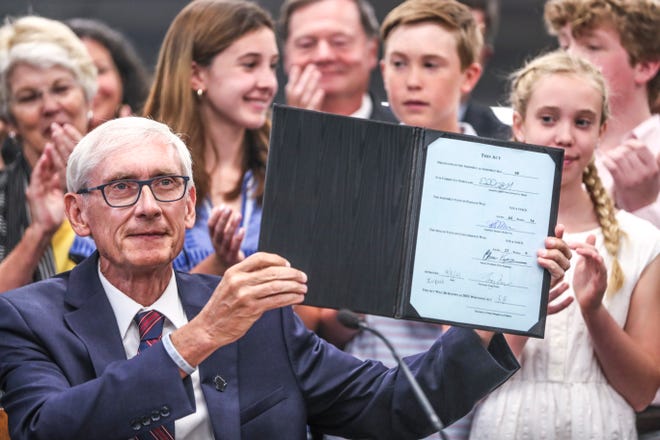 Photo of Wisconsin Governor Tony Evers holding up the signed state budget bill will people applauding in the background.