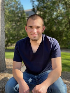 Photo of a young man in a blue shirt and jeans sitting on a rock.