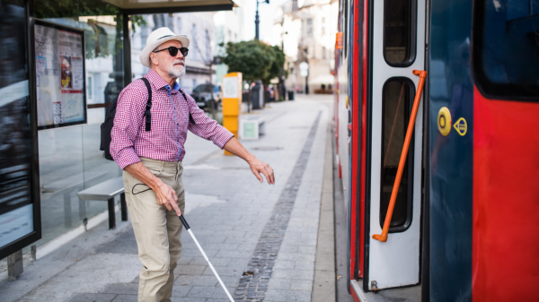 Man with a white cane getting on a bus.