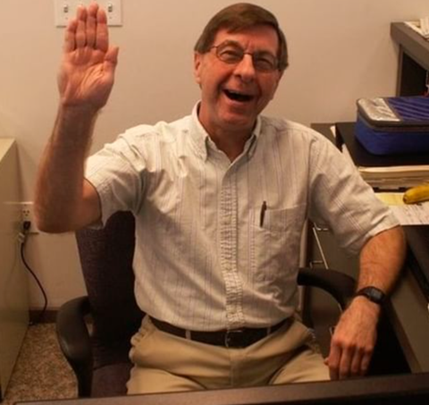 Ray Cubberly sitting at a desk waving goodbye