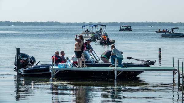 People sitting in a small motorboat and standing on a dock next to it