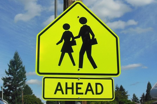 A yellow traffic sign showing a pair of pedestrians and the word ahead