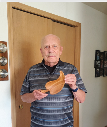 Chuck Fehl standing in front of a door holding a leaf-shaped wood carving