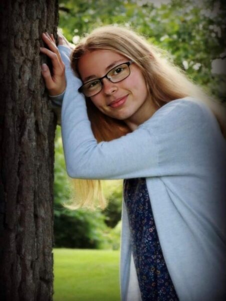 Grace Caine leaning against a tree smiling for the camera