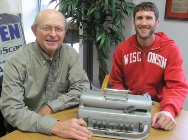 Joe Hodgson and Brent Perzentka sitting at a table with a braille machine
