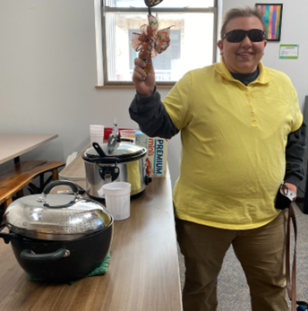 Rachel Pavone standing by a table with pots of chili holding up a decorated ladle