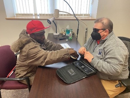 Rachel Pavone sitting across a table from a man using a braille labeler.