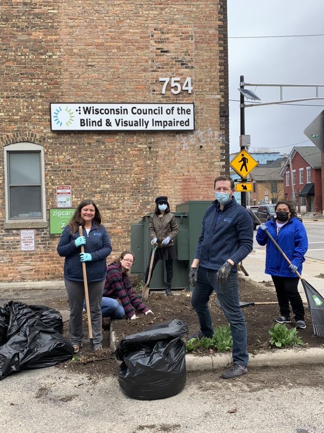 5 volunteers smile as they clean out a garden bed