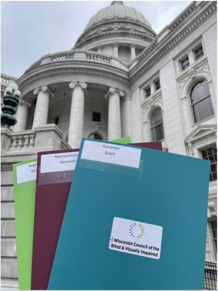 3 Advocacy Day folders held up in front of the Wisconsin Capitol.