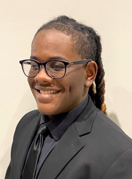 Portrait of Jayquan Jaeger wearing a suit and tie and smiling