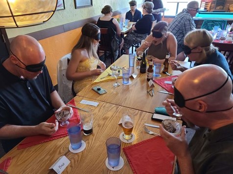 A table of blindfolded diners eating dessert and drinking beer