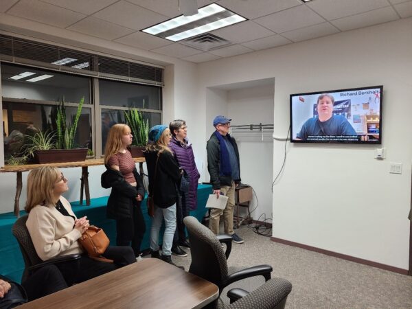 A group of people viewing a video on a wall-mounted monitor