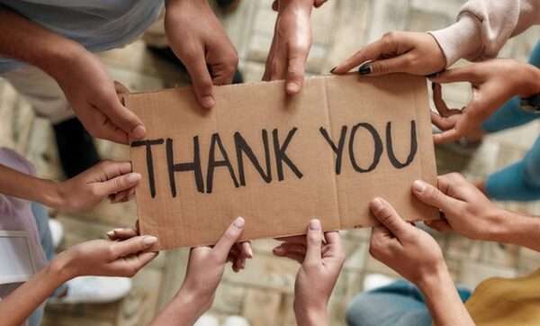 Five sets of hands holding a cardboard sign with the words Thank You written on it