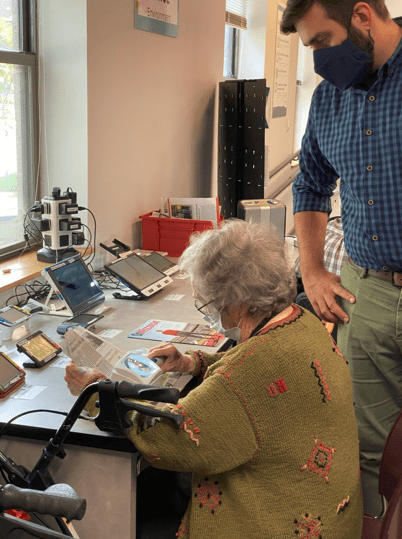 A woman sitting at a table using a handheld magnifier while a man stands behind her watching