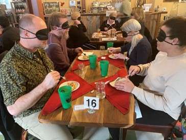 A group of blindfolded people sitting at a table eating a meal
