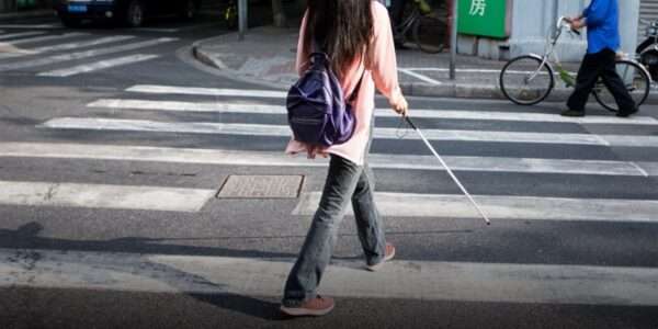 A person with a white cane walking in a crosswalk