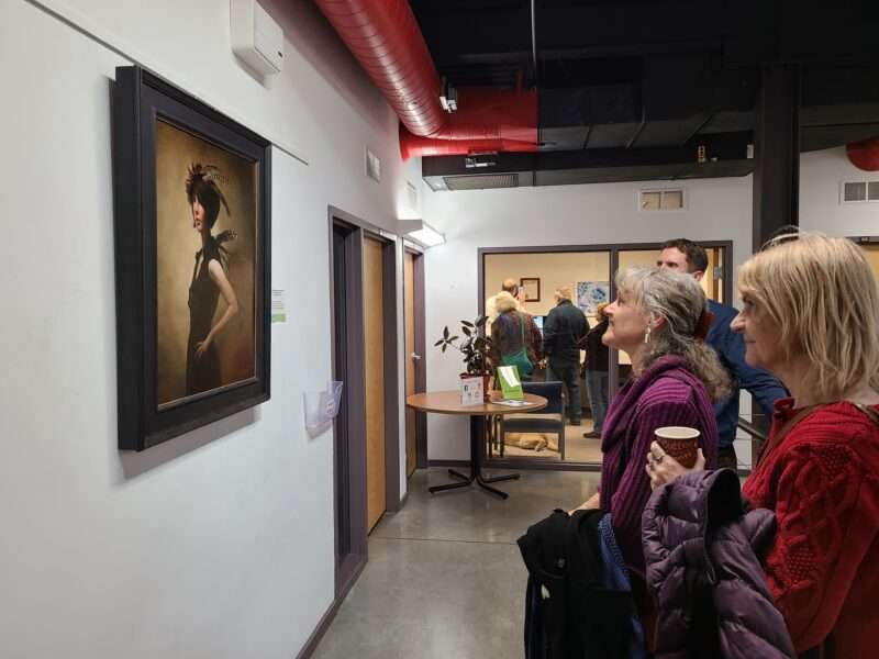 Three people examining a painting hanging on a wall in the Council office.