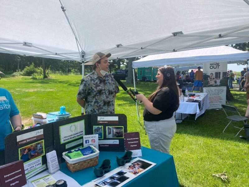 Nate Wegehaupt being interviewed by a radio reporter by the Council's booth at the Madison Disability Pride Festival.