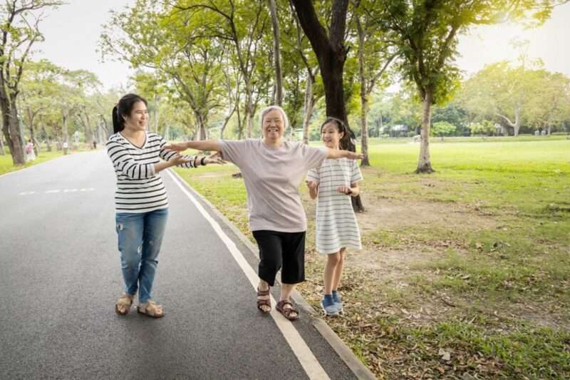 A smiling woman walking on the edge of a street with her arms held out for balance, flanked by two other people spotting her.