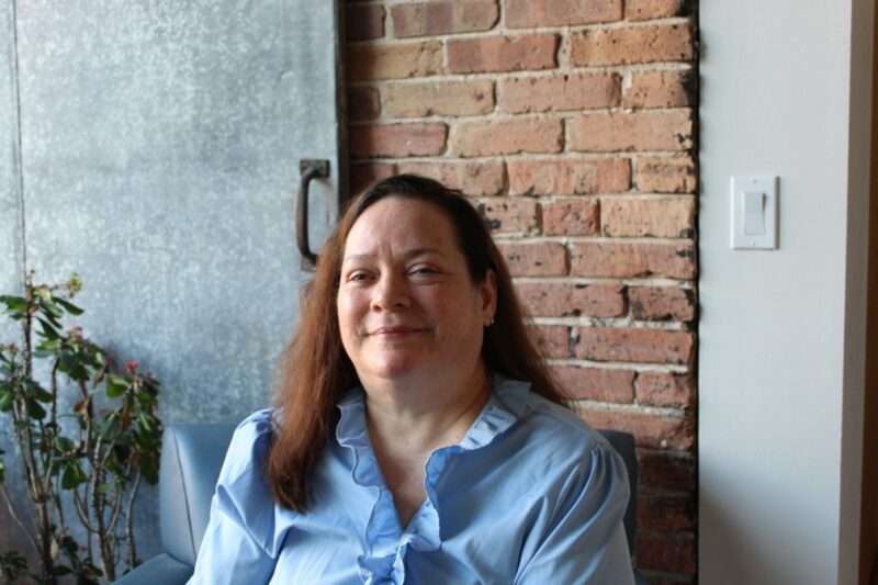 Photo of Susan Bosques in front of a brick wall and metal sliding door.