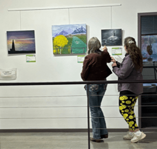 Two women examining paintings on a wall.