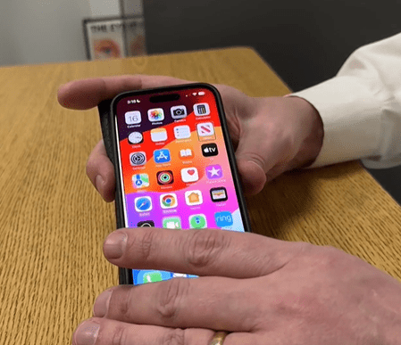 Screenshot from a video showing Jim Denham's hands demonstrating a VoiceOver gesture on an iPhone.