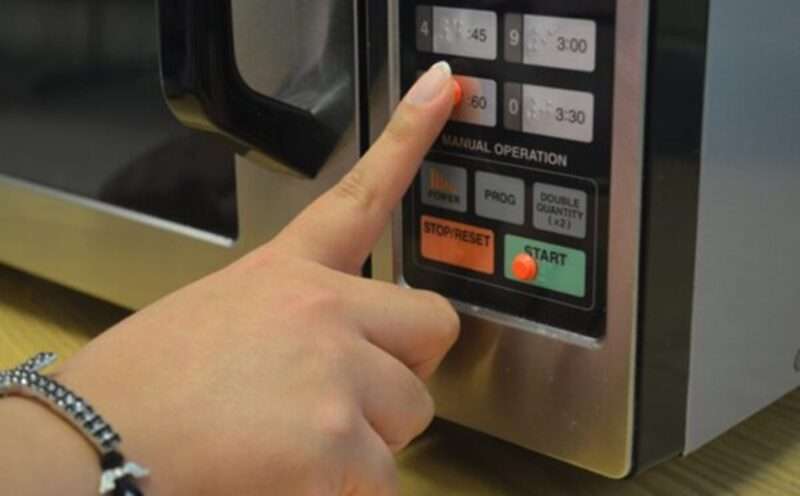 A hand pushing a button on a microwave oven marked with a bump dot