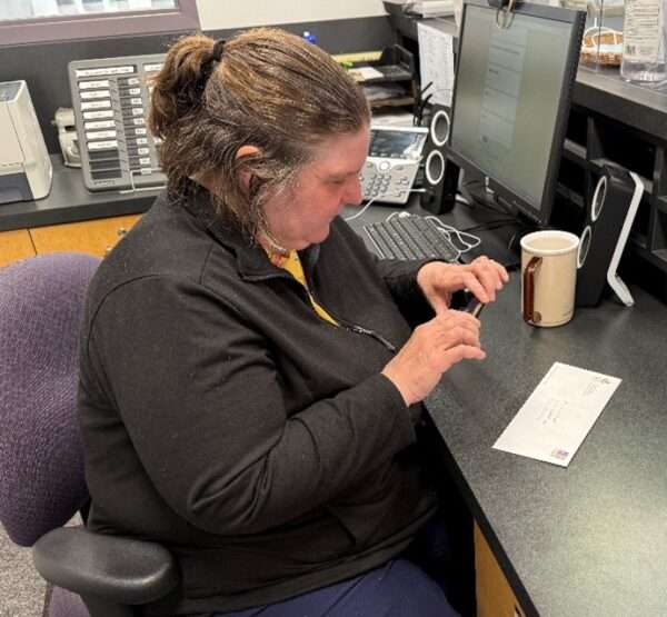 A light-skinned person sitting at a desk using a phone app to identify a piece of mail.