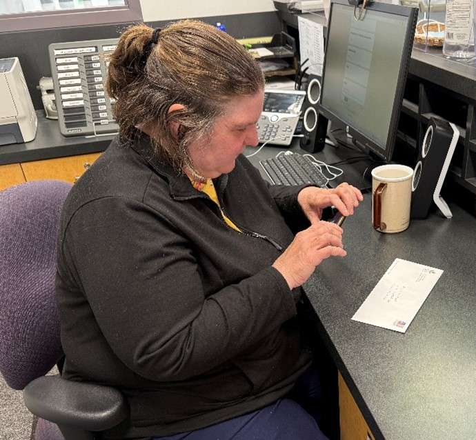 A light-skinned person sitting at a desk using a phone app to identify a piece of mail.