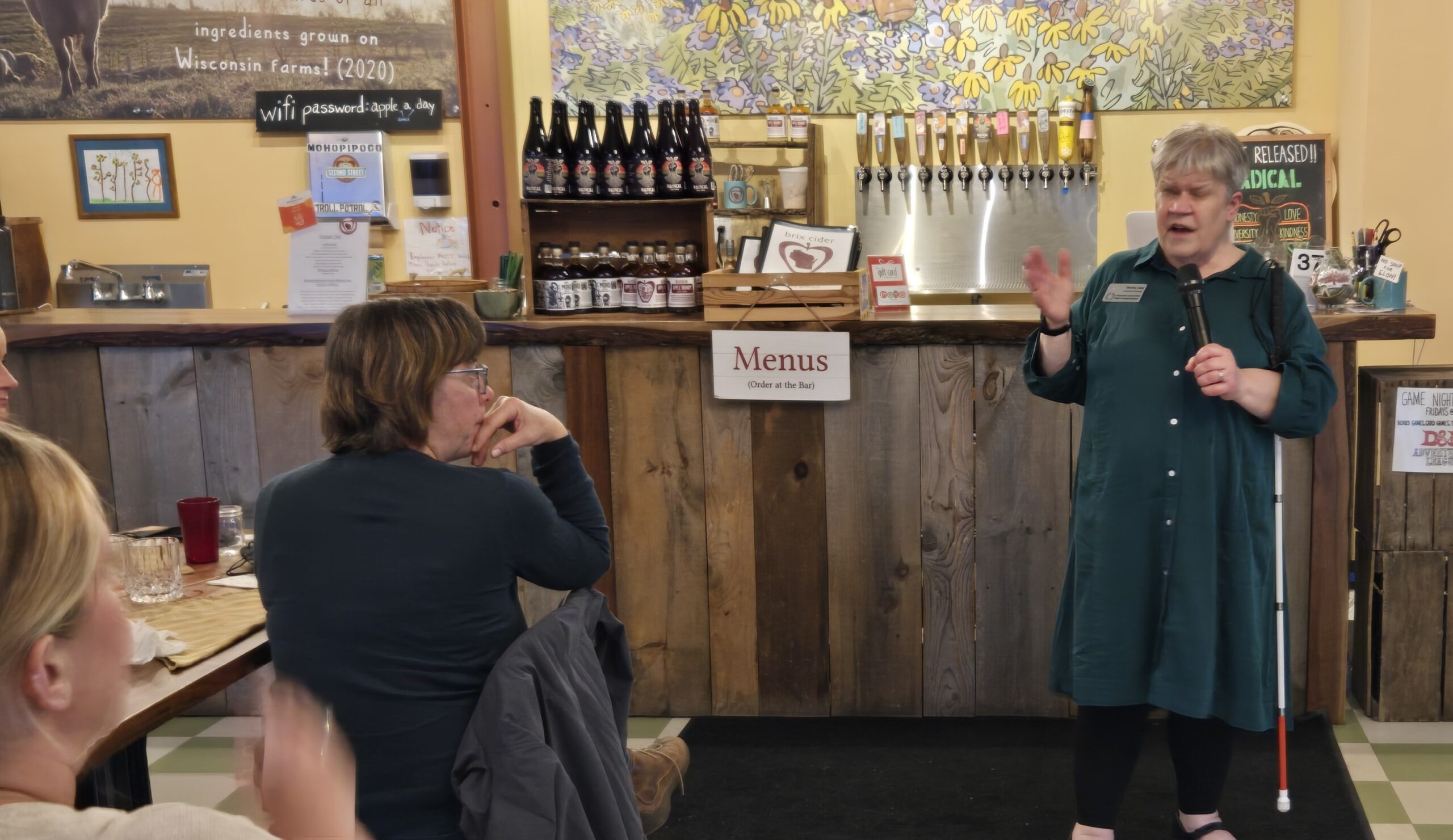 A women talking to a seated audience in a restaurant.