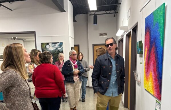 A group of people congregated in the Council office looking at art hanging on walls.