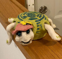 A turtle wearing a pink hat with a light green shell with dark green accents.