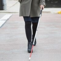 A person using a white cane in a crosswalk.