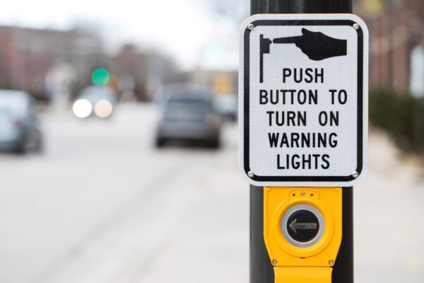 An Accessible Pedestrian Signal with large button and sign directing users to push to turn on warning lights.